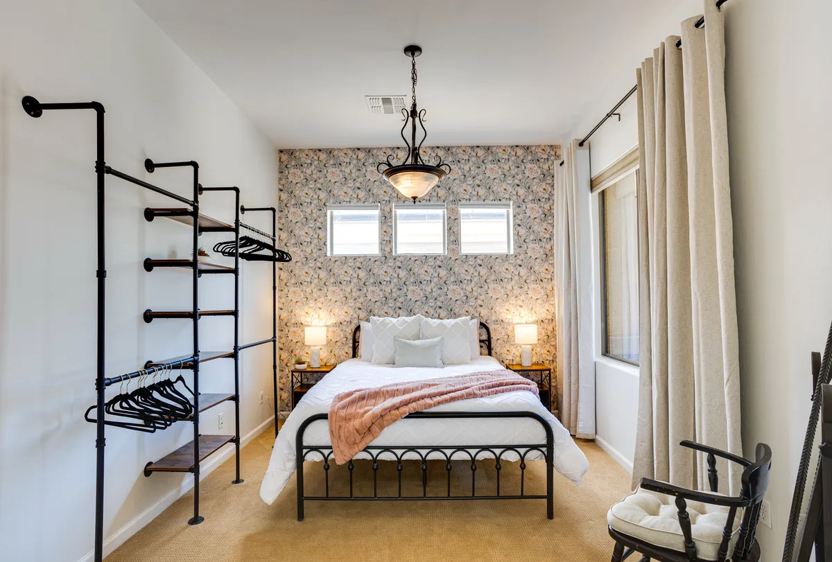 A cozy bedroom with a queen bed, vibrant floral wallpaper, elegant lighting, and nightstands. The space is warm and inviting, ideal for a restful sleep or quiet moments with a book.