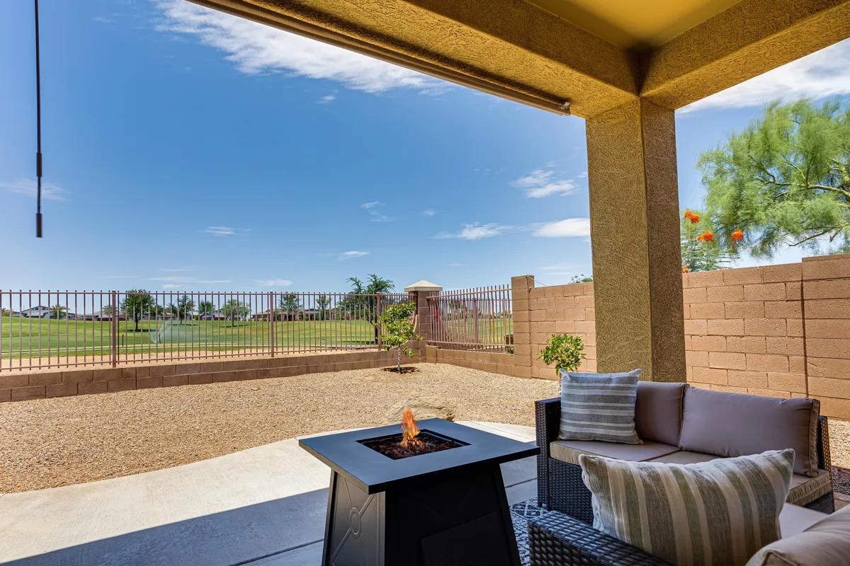 An inviting outdoor lounge area featuring a fire pit surrounded by comfortable seating, enclosed by a fenced yard and framed by landscape views. The setting is perfect for evenings spent under the stars or relaxed gatherings by the fire.