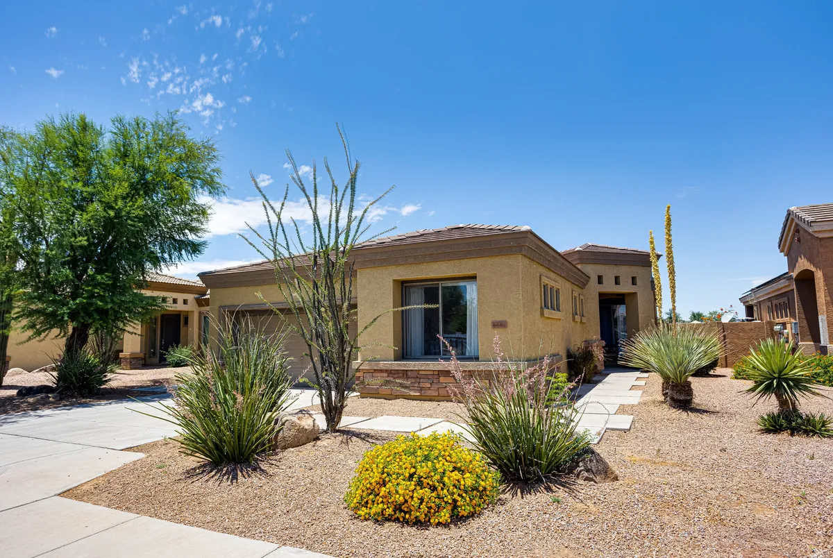 The photo features a welcoming front entrance framed by landscaped gardens and a pathway leading up to the door. The vibrant greenery and neat design evoke a sense of arrival and community, while also highlighting outdoor appeal.