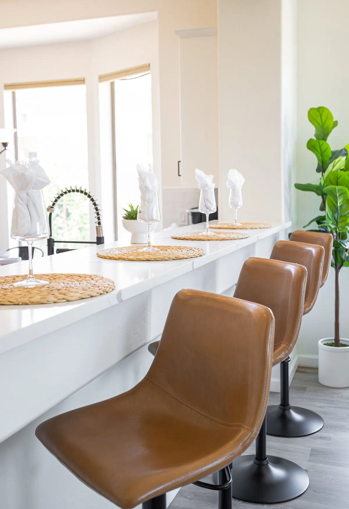 A bright and inviting dining area with bar stools and a thoughtfully set table, accented by lush plants. The space encourages casual dining, social gatherings, or simply enjoying morning coffee with friends.