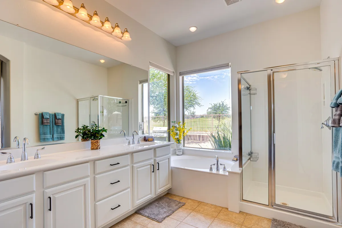 A luxurious bathroom with a large mirror, soaking bathtub, glass-enclosed walk-in shower, and a window offering natural light. The space is designed for calm and relaxation, with elegant finishes and spa-like ambiance.