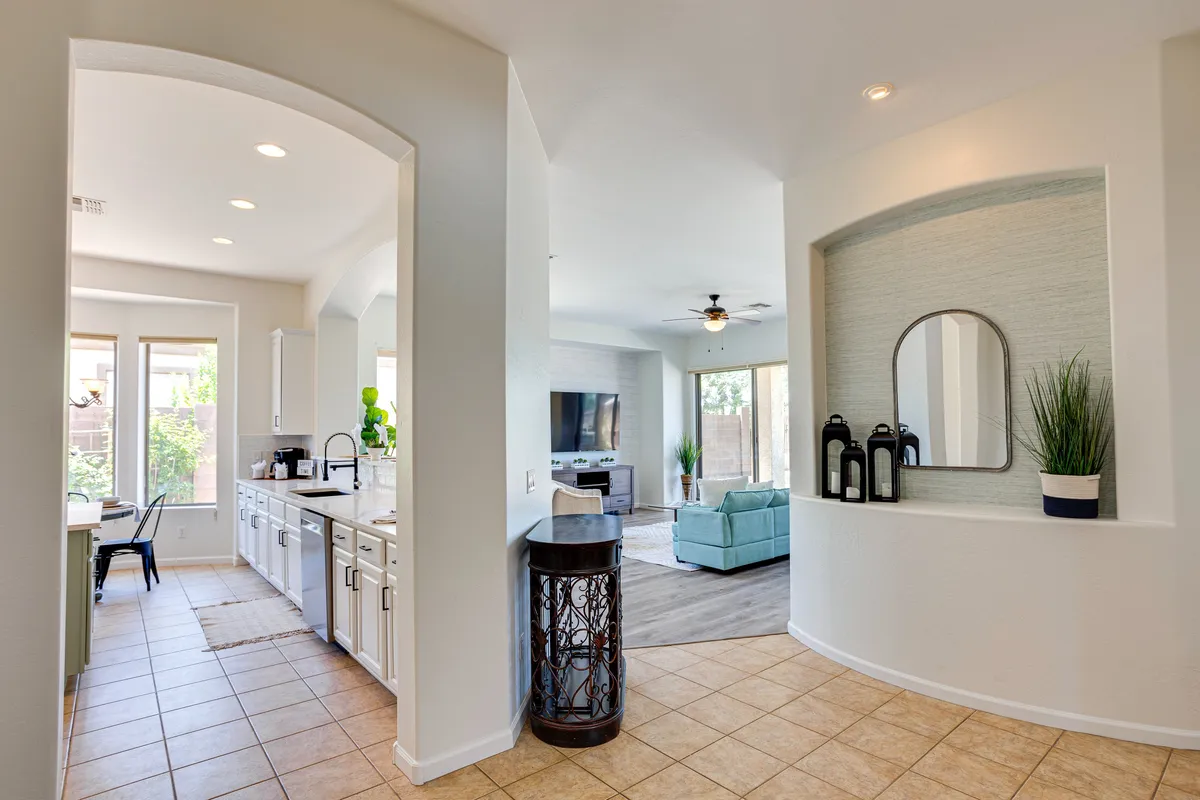A bright, inviting space where the kitchen and living area come together. Decorative touches like a stylish mirror, tall plants, and lanterns add warmth. Both areas are visible, showing the ease of movement and interaction between cooking, dining, and lounging.
