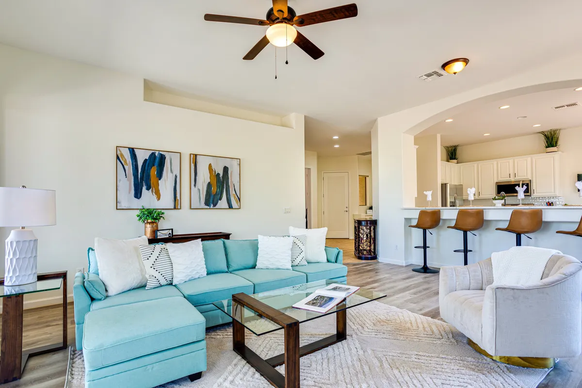 This image features a spacious interior with a turquoise sectional couch, wooden coffee table, abstract wall art, and bar stools at the kitchen counter. The visual connection between the family room and kitchen is highlighted, creating a welcoming space for both relaxation and socializing.