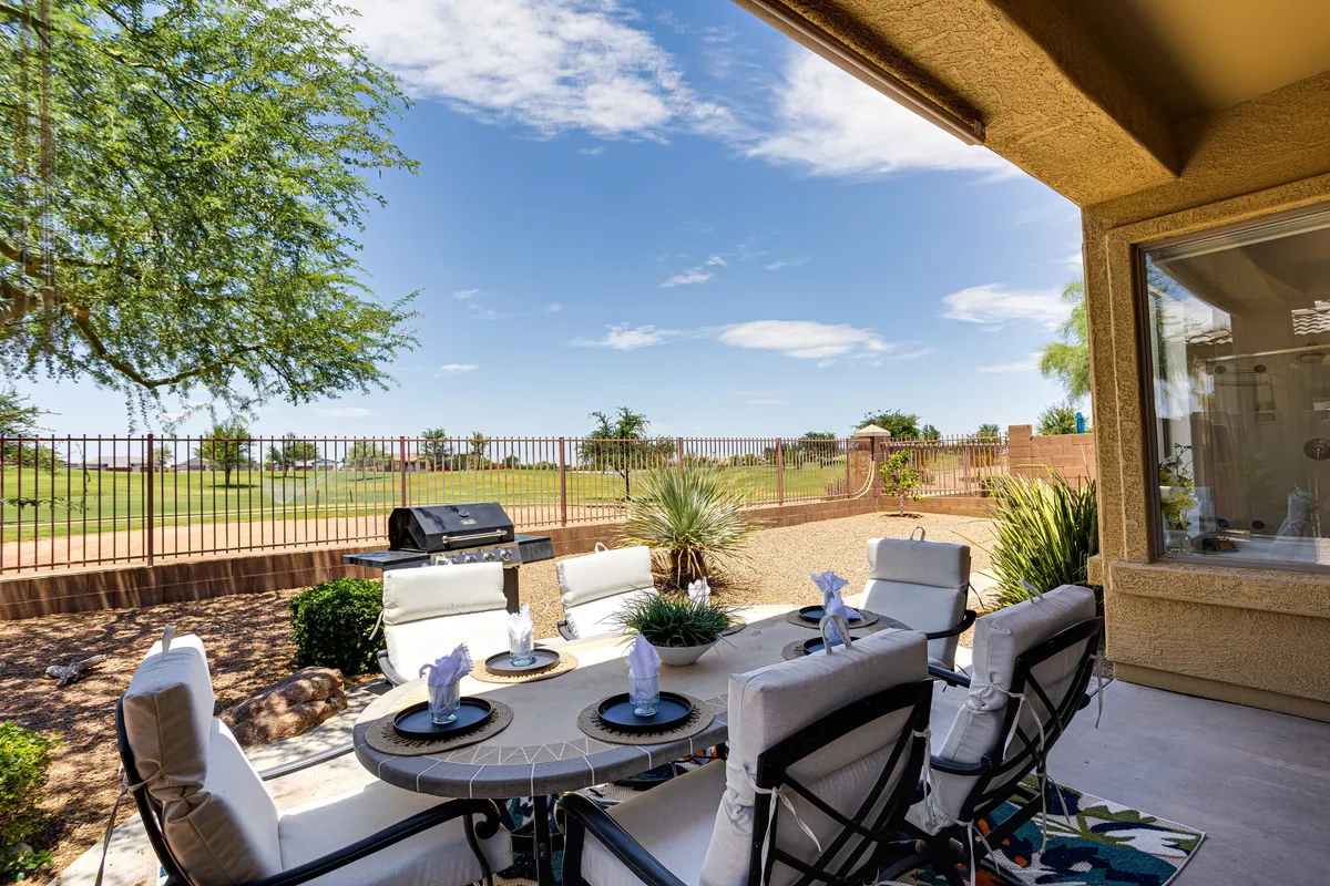 This image features an inviting outdoor dining table set under open sky, with a grill nearby and a landscape view stretching beyond. The setting radiates a sense of relaxed community living, perfect for gatherings, al fresco meals, or simply enjoying the sunset.