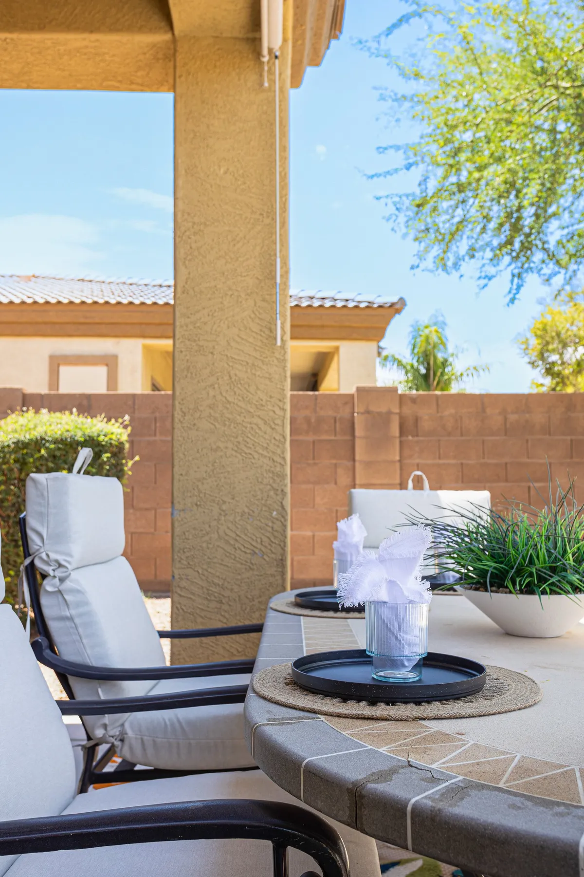 An outdoor table is set for dining, nestled among green plants. The seating area offers a relaxed, welcoming vibe, suggesting the perfect spot for a family meal or gathering with friends under open skies.