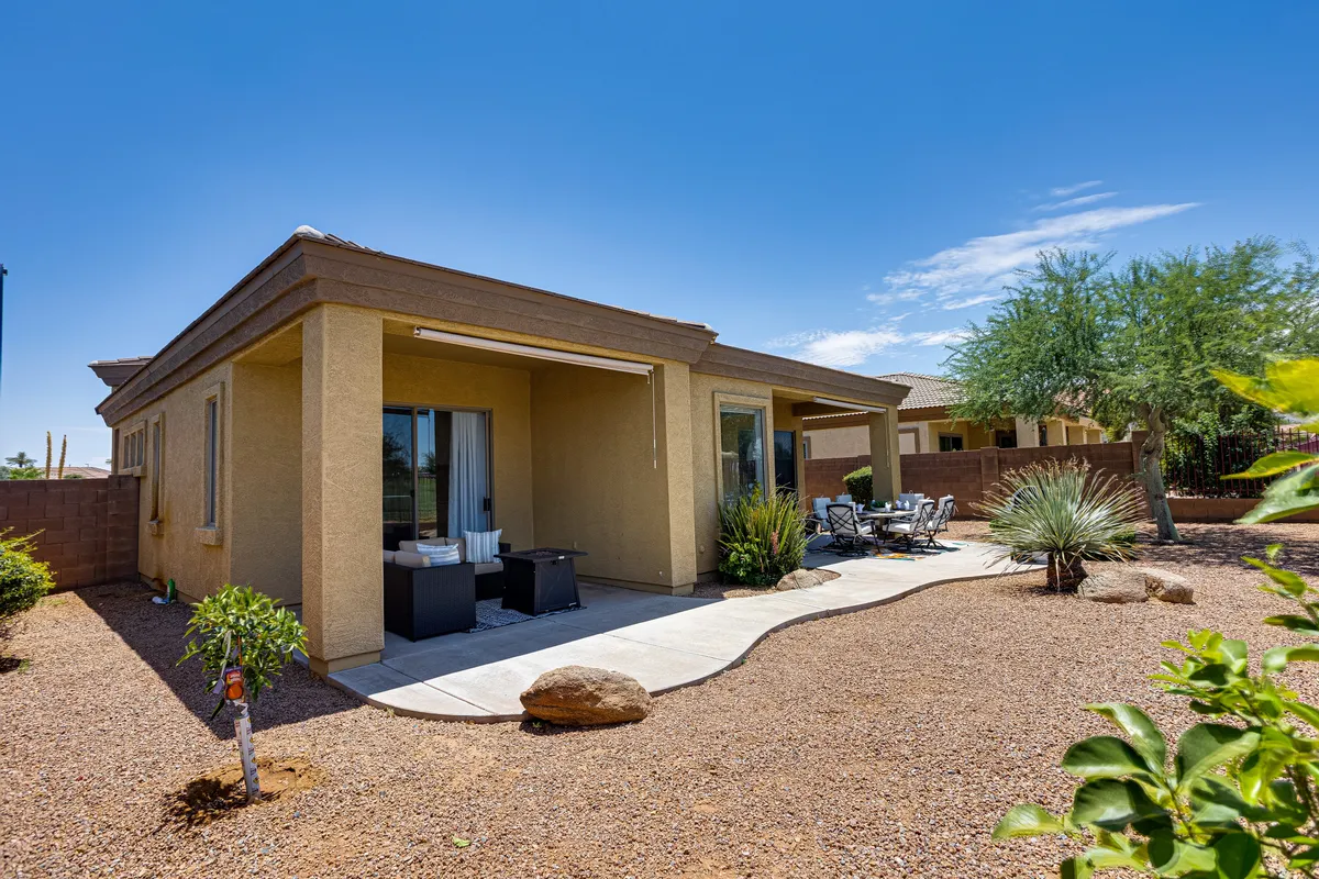This image showcases a comfortable patio seating area surrounded by lush greenery and rock landscaping. The outdoor setting is designed for relaxation, social gatherings, and dining, with the backdrop suggesting open views and tranquil outdoor living.